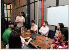 Builders with laptops around a table at a 3percentclub workshop while a speaker presents